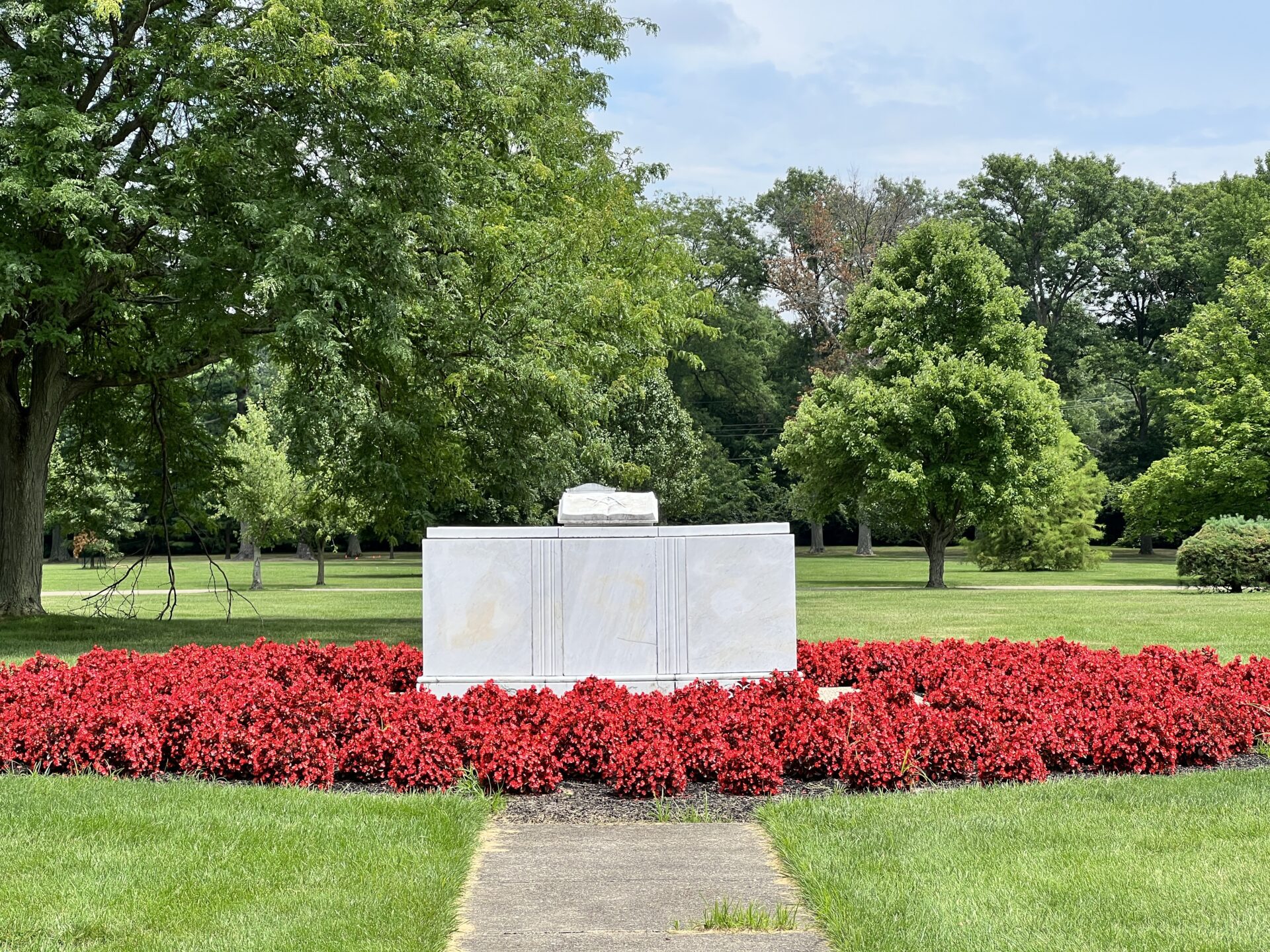 An outdoor photo of a stone sculpture of the Bible in the center of red flowers