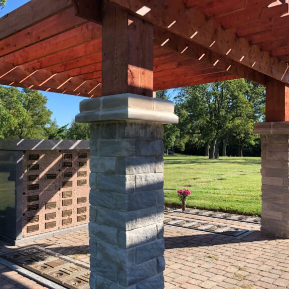 Photo of a brick pergola with a red wood stained roof and memorial plaques within the ground and wall
