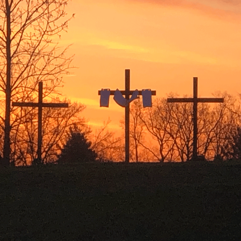 Photo of three crosses in front of an orange/yellow/pink sunrise at the Easter Sunrise Service