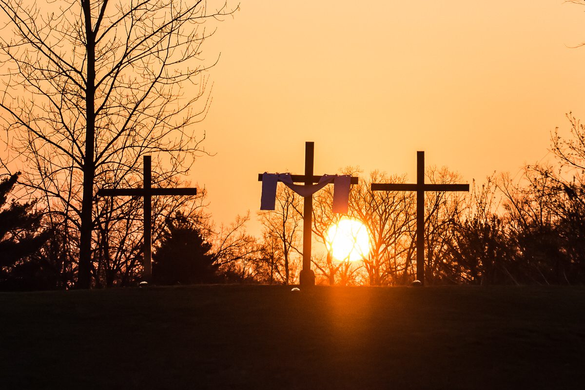 Image of three wooden crosses at the top of a hill with the sunrise behind them
