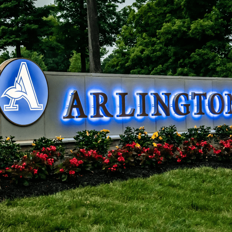 photo of Arlington Memorial Gardens sign - the Arlington Memorial Gardens name backlit by blue lights on a concrete block behind a garden