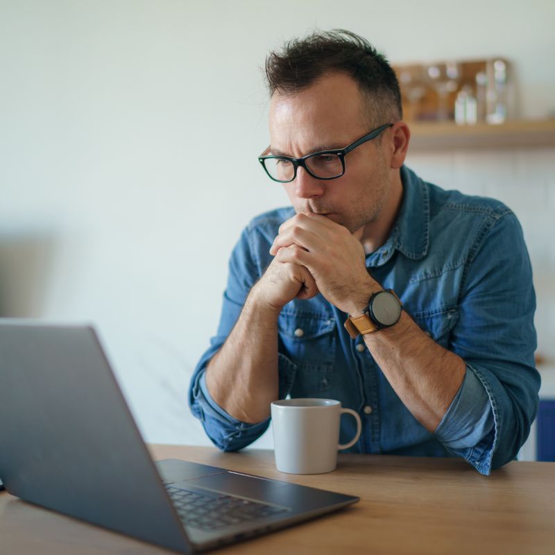 photo of a man holding his hands together under his chin while looking at his computer with a contemplative look