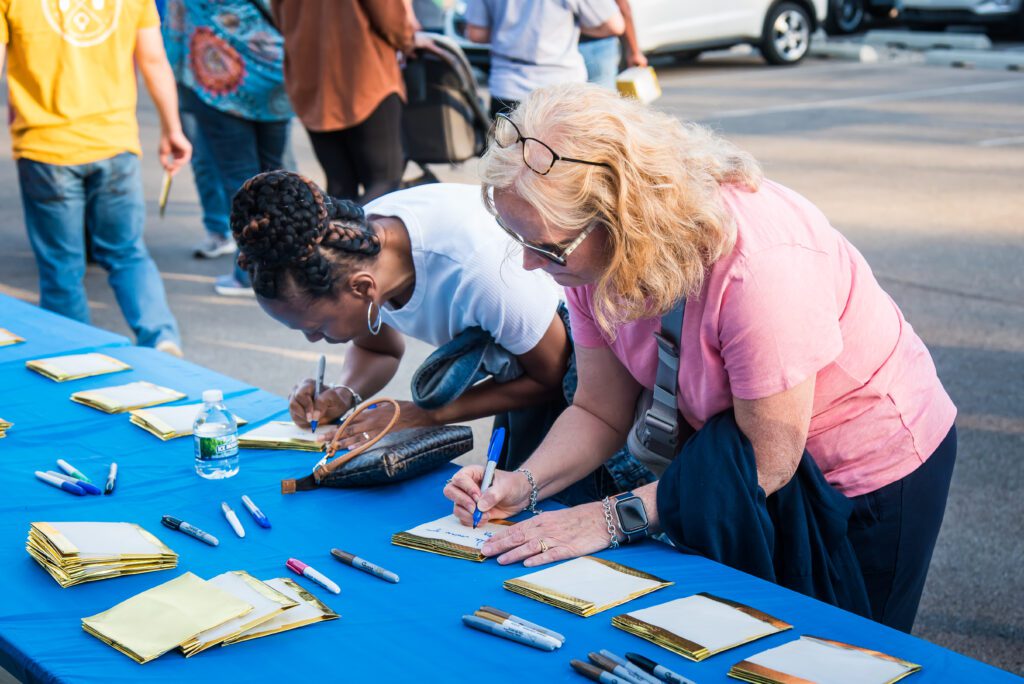 Photo of two women writing notes on white paper memory lanterns