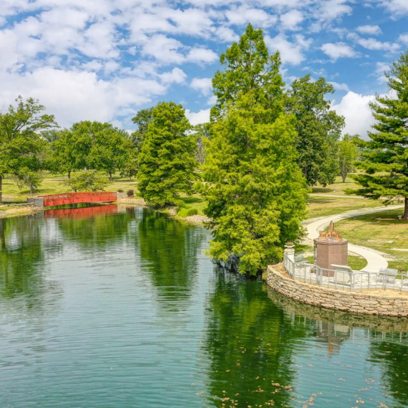 photo of a pond with a red bridge over it in the distance with trees lining the shoreline