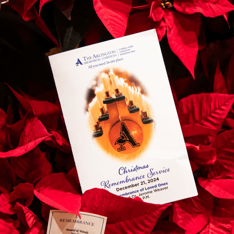 Image of a pamphlet from the Christmas Remembrance Service 2024 sitting in a bed of poinsettia flowers