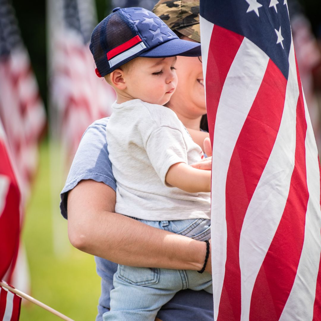 Guest at Field of Memories 2025 holding a baby while looking at an American flag