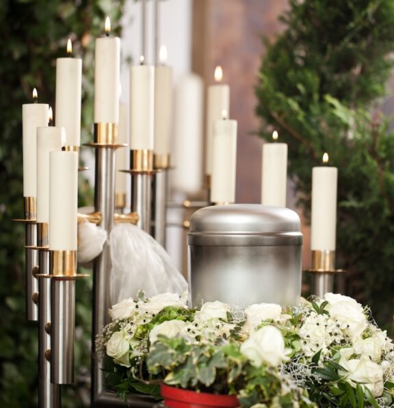 Urn for cremation surrounded by flowers and lit white candles funeral and cemetery